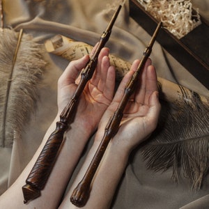 May include: Two wooden wands with dark brown and light brown wood grain. The wands are held in the hands of a person.