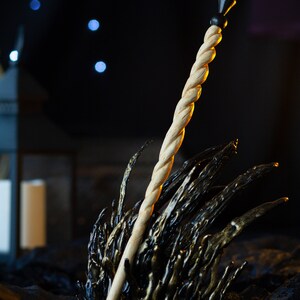 May include: A wooden wand with a black tip, resting on a black and gold metal throne-like object. The wand is twisted and has a smooth, polished finish.
