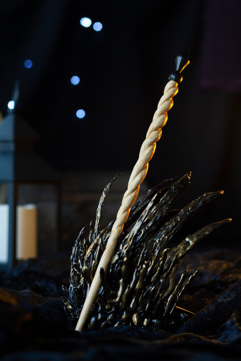 May include: A wooden wand with a black tip, resting on a black and gold metal throne-like object. The wand is twisted and has a smooth, polished finish.