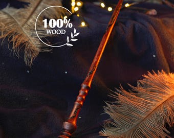 May include: A wooden wand with a dark brown finish and intricate carvings. The wand is lying on a dark fabric background with a feather and string lights.