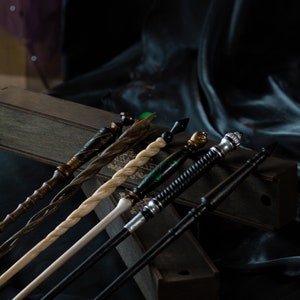 May include: A set of six wooden wands with different colored tips and designs. The wands are arranged in a wooden box with a black velvet background.