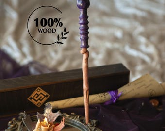 May include: A handcrafted wooden wand with a purple handle and a natural wood shaft. The wand has a carved design and is displayed with a scroll, a candle, and a box. The text "100% WOOD" is also visible.