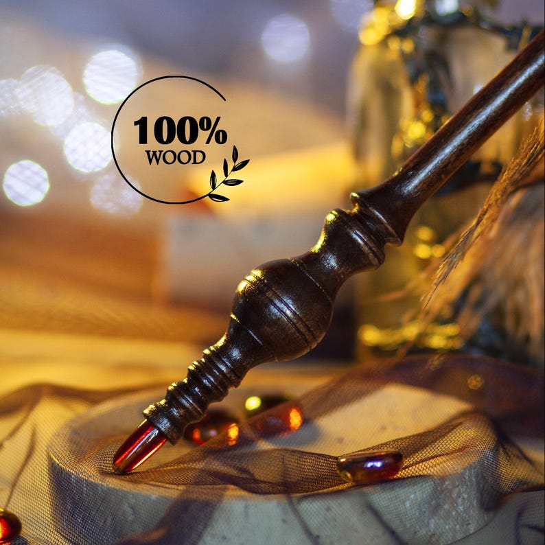May include: A dark brown wooden wand with intricate carvings and a red crystal tip. The wand is labeled "100% WOOD" and is set against a blurred background with warm lighting. The wand is a magical item.
