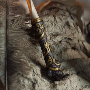 May include: A wooden wand with gold accents and intricate carvings. The wand is decorated with a leafy pattern and has a pointed tip.