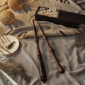 May include: Three wooden wands with intricate details, lying on a brown fabric surface. The wands are arranged in a row, with the tips pointing towards the right side of the image. The fabric has a subtle texture and a warm, inviting tone.