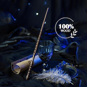 Puede incluir: Una varita de madera con un mango en espiral y un diseño detallado, un vaso azul, un pergamino, una pluma y un espejo están dispuestos sobre una superficie oscura. Incluye el texto "100% WOOD".