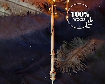 May include: A wooden wand with a light brown finish and dark brown accents. The wand is on a dark blue fabric background with white feathers. The text "100% WOOD" is visible in the image.