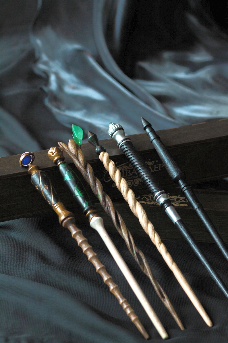 May include: Six wooden wands with different colored tips and designs. The wands are arranged in a row on a dark surface. The wands are all about 12 inches long.