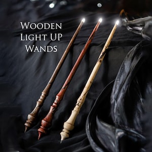 Puede incluir: Tres varitas mágicas de madera iluminadas con intrincadas tallas y puntas brillantes. Las varitas son en tonos marrón, rojo y crema, sobre un fondo oscuro y texturizado. El texto "WOODEN LIGHT UP WANDS" se muestra en blanco.