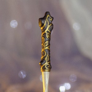 May include: A wooden wand with a dark brown finish and gold accents. The wand is decorated with a vine-like pattern.
