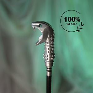 May include: A silver-colored snake-shaped bottle stopper with a detailed design. The stopper has a black stem and the text "100% WOOD" in a circle. The snake's mouth is open, revealing a small green gem.