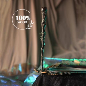 May include: A dark wooden wand with silver wire detailing. The wand has a textured, natural look with a curved design. The image includes the text "100% WOOD" within a white circle.