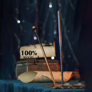 Op de afbeelding: Twee houten toverstokken, één met een bolvormige top en de andere met geëtste ontwerpen, worden getoond. De toverstokken zijn bruin en grijs, met een donkere achtergrond en de tekst "100% WOOD". De toverstokken staan op een decoratieve standaard.