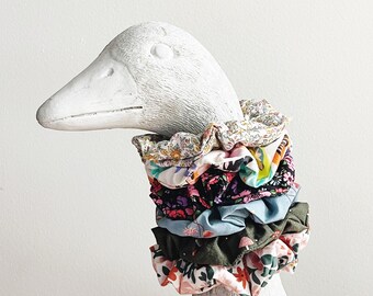 May include: A stack of five colorful fabric scrunchies with floral patterns. The scrunchies are arranged on a white goose figurine.