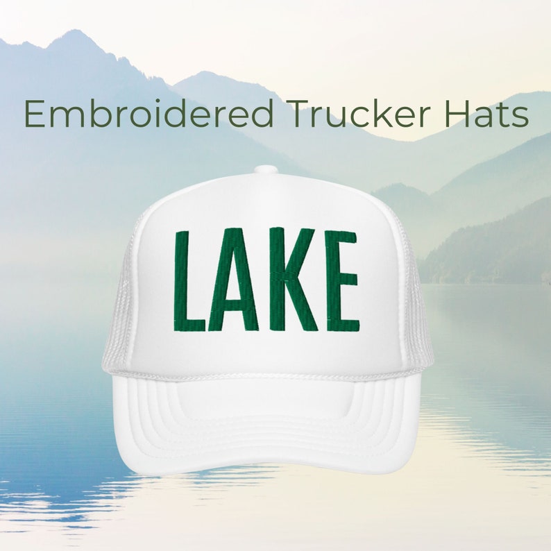 Może przedstawiać: Biała czapka trucker z haftowanym zielonym napisem "LAKE" z przodu.