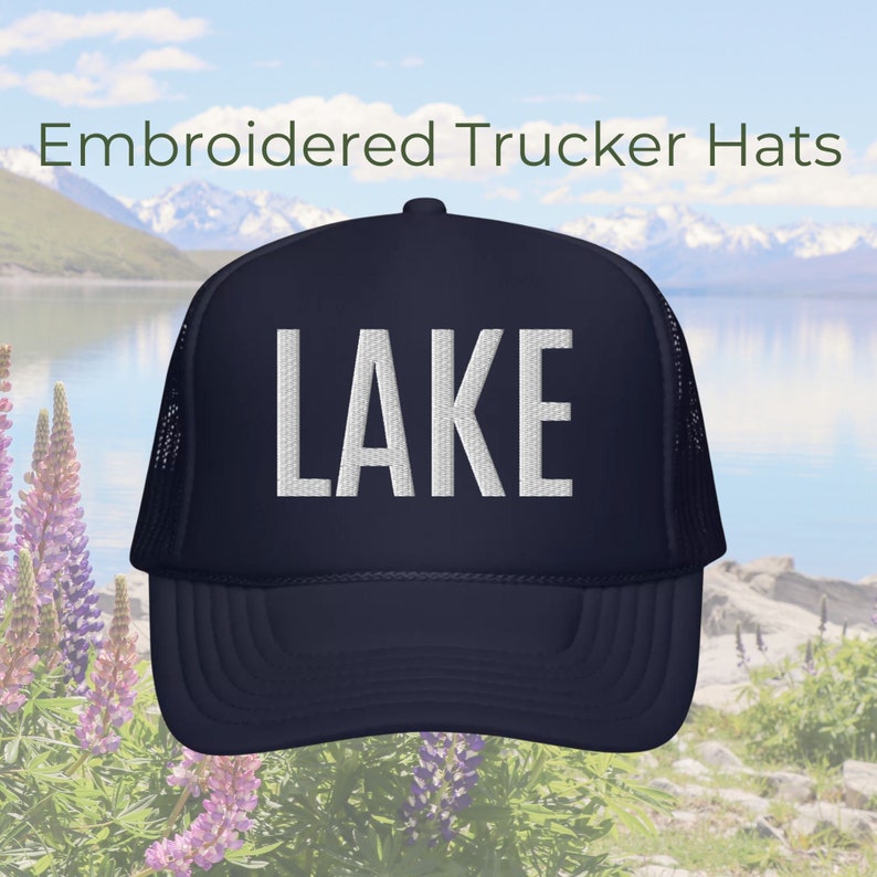 Może przedstawiać: Czapka trucker w kolorze granatowym z siateczką z tyłu w kolorze białym. Na przodzie czapki wyszyte jest białe słowo "LAKE".