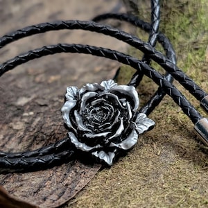 May include: A black leather bolo tie with a silver rose pendant. The rose is detailed and has a realistic look.