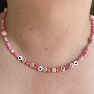 May include: A pink and white beaded necklace with the word "SILK CHIFFON" spelled out in gold letters. The necklace has small black hearts between each letter.