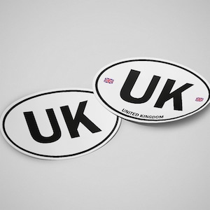 Könnte beinhalten: Zwei weiße ovale Aufkleber mit schwarzem Text, der "UK" und "UNITED KINGDOM" lautet. Jeder Aufkleber hat auf beiden Seiten des Textes eine kleine Union Jack-Flagge.