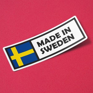 以下が含まれることがあります： 黒枠の白いステッカーに、黒い文字で「Made in Sweden」と書かれています。ステッカーには、青い背景に黄色の十字架が描かれたスウェーデンの国旗がデザインされています。