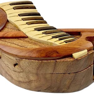 May include: A wooden piano-shaped puzzle box with a hinged lid and a separate piece that fits into the box. The box is made of light and dark wood and has a natural finish.