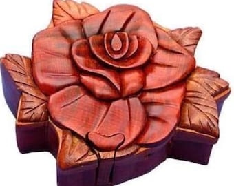 May include: A wooden rose-shaped box with intricate carvings. The box is primarily reddish-brown with darker purple accents on the base and leaves. The rose petals and leaves are detailed with visible wood grain.