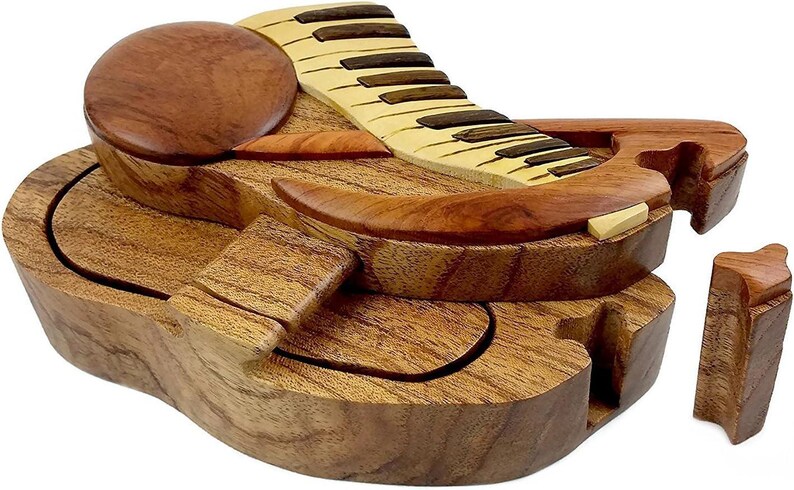 May include: A wooden puzzle box shaped like a grand piano with a hinged lid and multiple interlocking pieces. The box is made of light and dark wood and has a natural finish.