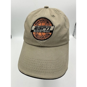 May include: A beige baseball cap with an embroidered logo featuring the text "NCAA Basketball" and "ESPN" with a basketball graphic.