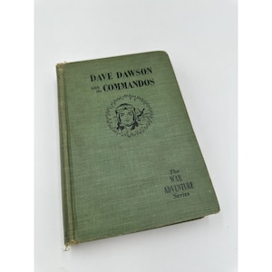 May include: A green book titled "Dave Dawson with the Commandos" with a black and white illustration of a man in a pilot's helmet and goggles. The book is part of "The War Adventure Series".