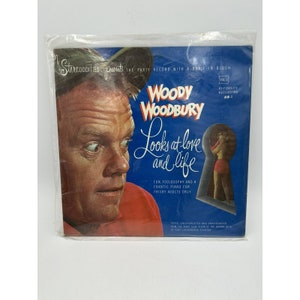 May include: A vintage record cover featuring a man in a red shirt and a woman in a red bikini. The cover is titled "Woody Woodbury Looks at Love and Life" and features the text "Fun, Foolosophy and a Frantic Piano for Frisky Adults Only".