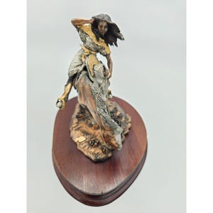 May include: A bronze sculpture of a Native American woman riding a horse. The sculpture is on a wooden base and is signed "C.A. Rodell".