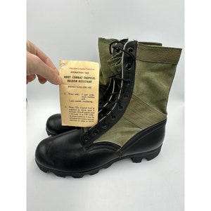 May include: A pair of black and green combat boots with a tag that reads "Boot Combat Tropical Mildew Resistant". The tag includes instructions for use, including wearing socks and incles.