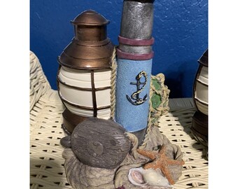 May include: A nautical themed decorative figurine with a brown lantern, a blue and gray telescope, a rope, a starfish, and a seashell.