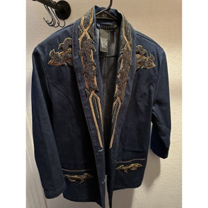 May include: A dark blue denim jacket with a beaded collar and gold embroidery. The jacket has a single button closure and two pockets. The label on the jacket reads "Le Diffusion".