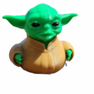 May include: A 3D-printed figurine of a character with large green ears, black eyes, and a tan robe. The figure is a stylized representation of a popular science fiction character. The figurine is a solid color and appears to be made of plastic.