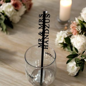 以下が含まれることがあります： 黒いプラスチック製のストローに「MR & MRS HANDZUS」の文字が印刷されています。ストローは、底に「Best Day Ever」の文字が印刷された透明なグラスに入っています。
