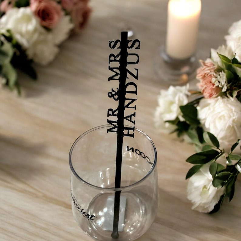 以下が含まれることがあります： 黒いプラスチック製のストローに「MR & MRS HANDZUS」の文字が印刷されています。ストローは、底に「Best Day Ever」の文字が印刷された透明なグラスに入っています。
