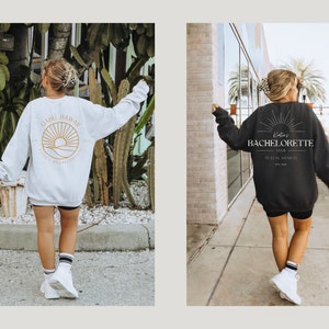 May include: Two women wearing sweatshirts with different designs. The first sweatshirt is light grey with a graphic of a sunset and the text "Oahu Hawaii" on the back. The second sweatshirt is black with the text "Katie's Bachelorette Club Tulum, Mexico Est. 2023" on the back.