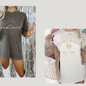 May include: Two women wearing oversized t-shirts with different designs. The first shirt is grey with the text "Katie's Bachelorette Club Tulum, Mexico" in gold lettering. The second shirt is white with the text "Bora Bora Girls Club" in gold lettering and a seashell graphic.