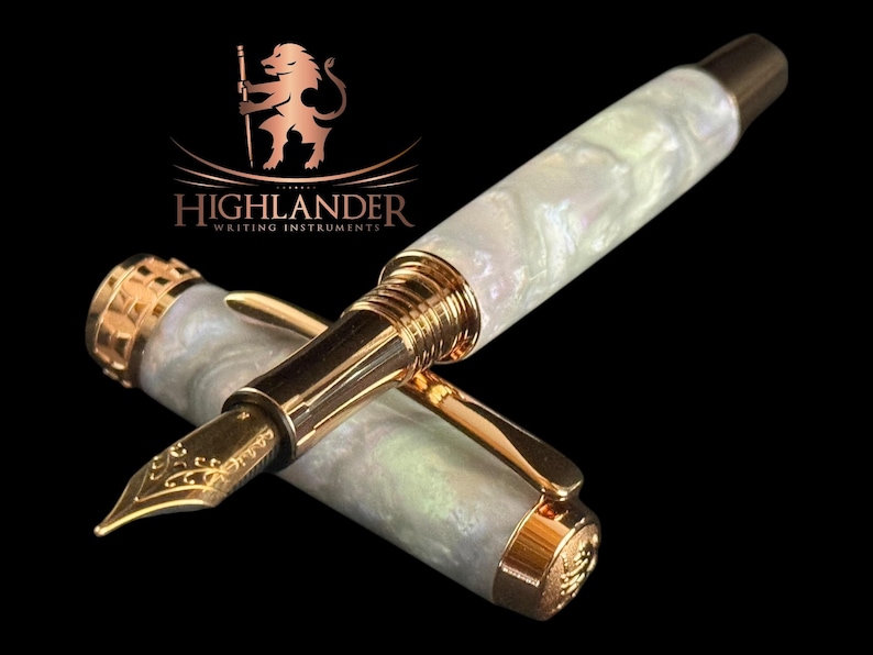 May include: A high-end fountain pen featuring a pearlescent white barrel and gold-coloured detailing. The nib is gold-coloured and has an ornate design. The pen is from Highlander Writing Instruments, as shown by the logo.