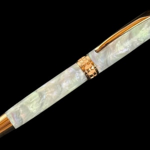 May include: A fountain pen with a pearlescent white barrel and gold-coloured accents. The pen has a gold clip and a decorative gold band near the centre. The pen's tip and end cap are also gold, creating a sophisticated writing instrument.