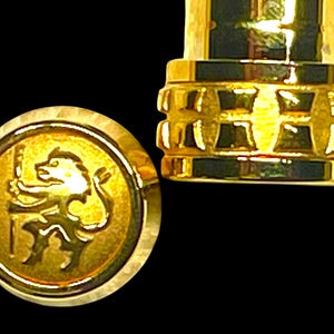 Puede incluir: Primer plano de un tap&oacute;n de botella dorado con un emblema de le&oacute;n. El tap&oacute;n tiene un dise&ntilde;o detallado y texturizado. El fondo es negro, lo que resalta el color dorado del tap&oacute;n.