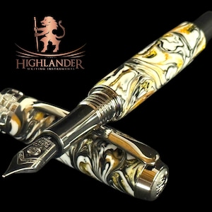 Puede incluir: Una pluma estilogr&aacute;fica de lujo con un patr&oacute;n veteado en negro, blanco y amarillo. La pluma tiene un plum&iacute;n y detalles plateados, y la marca "Highlander Writing Instruments" es visible.