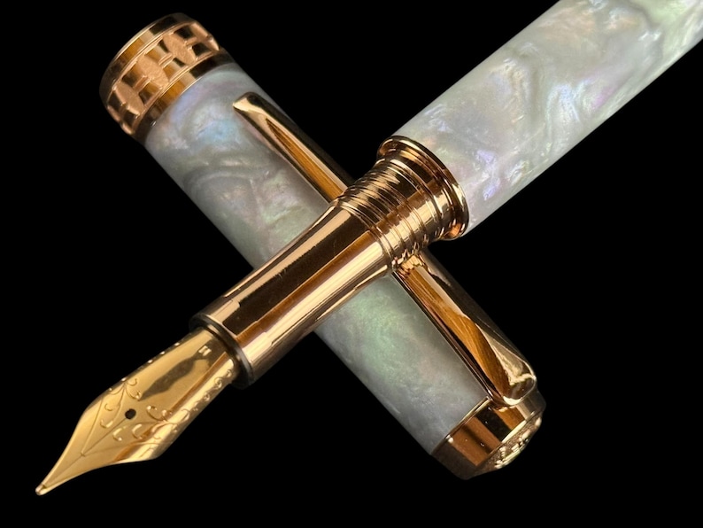 May include: A luxury fountain pen with a gold nib and accents. The pen has a pearlescent white barrel and cap, and a gold clip. The nib is intricately detailed. The pen is set against a black background.