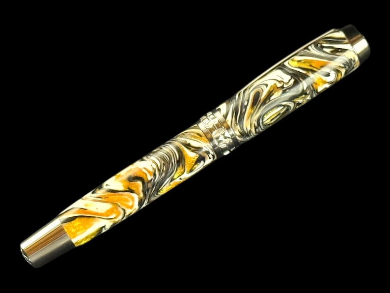 Puede incluir: Una pluma estilogr&aacute;fica de lujo con un patr&oacute;n arremolinado de oro, blanco y negro. La pluma tiene un plum&iacute;n y detalles plateados. El fondo es negro.