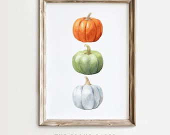 May include: A framed watercolor print featuring three stacked pumpkins in a vertical arrangement. The top pumpkin is orange, the middle is light green, and the bottom is pale blue. The text THE PROUD PAPER Handcrafted Watercolors is below.