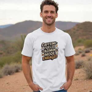 May include: White t-shirt with the text "Caffeine Fueled Admin Mode Enraged" in a black and yellow design. The shirt features coffee cups, lightning bolts, and starburst graphics. The person is wearing blue jeans.