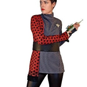 May include: A person in a Star Trek-themed costume. The outfit includes a red and black patterned top, a black belt, and black leggings. The person is holding a prop weapon and wearing black, knee-high boots.