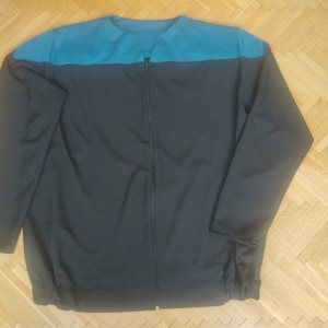 Può includere: Giacca con zip a maniche lunghe, grigio scuro, con carrè turchese sulle spalle. La giacca ha un design semplice e funzionale, con taglio dritto e zip a tutta lunghezza. Le maniche sono lunghe e i polsini elasticizzati.