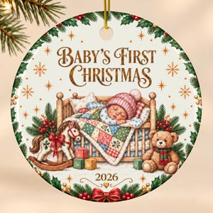 May include: A round ceramic Christmas ornament featuring the text Baby's First Christmas and 2026. The illustration shows a baby sleeping in a wooden crib under a colorful patchwork quilt, accompanied by a rocking horse, a teddy bear, and holly.